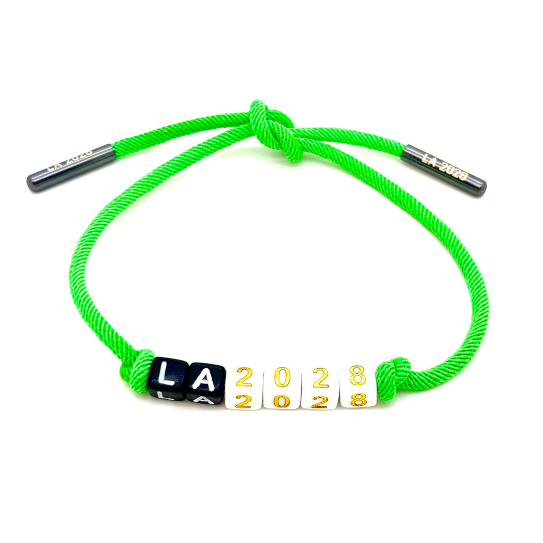 A bright green braided cord bracelet with adjustable sliding metal ends and a central beaded section spelling out 'LA 2028' in black, white, and gold lettering, shown on a plain white background.